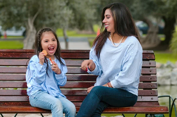 Madre y su hijita sentadas en un banco comiendo una galleta — Foto de Stock