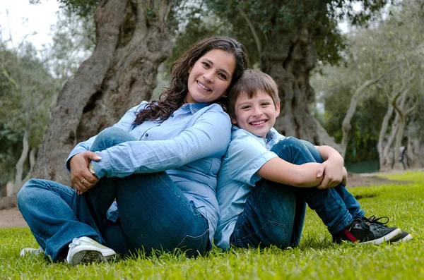 Mom and son sitting on green grass in green park. Concept of happy family relations