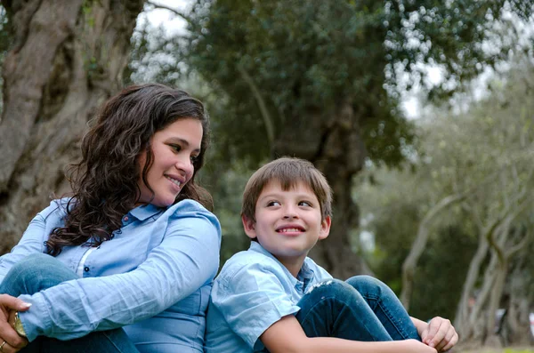 Moeder en zoon zittend op groen gras in groen park. Concept van gelukkig familierelaties — Stockfoto