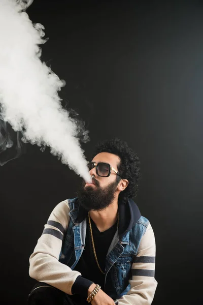 Joven con barba vapeando un cigarrillo electrónico hacia arriba. Vaporizador de humo Vaper hipster . — Foto de Stock