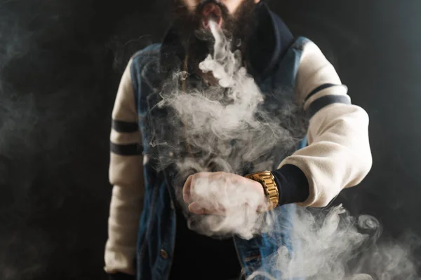 Young man with beard throwing a cloud of steam. Black background. Vaping an electronic cigarette — Stock Photo, Image