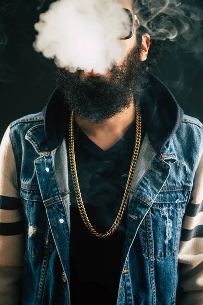 Young man with beard throwing a cloud of steam. Black background. Vaping an electronic cigarette