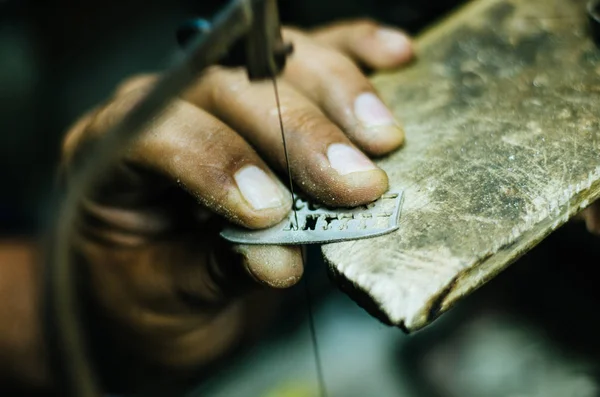 Manos mans orfebre trabajo en una pieza de plata con una sierra de metal en la mesa de trabajo, de cerca, enfoque seleccionado —  Fotos de Stock