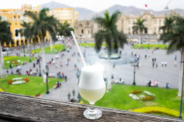 Pisco sour homemade cocktail with the background of the main square of Lima — Stock Photo, Image