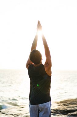 Genç adam plajda yoga yapıyor.