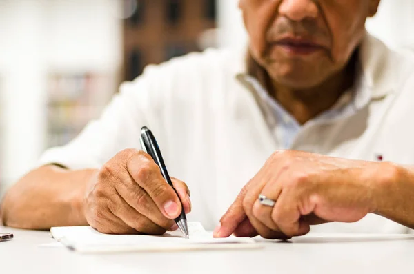 Serious senior man sitting on a library bench writing in his book. — Stock Photo, Image