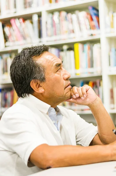 Задумчивый старшеклассник с рукой на подбородке смотрит в библиотеку — стоковое фото