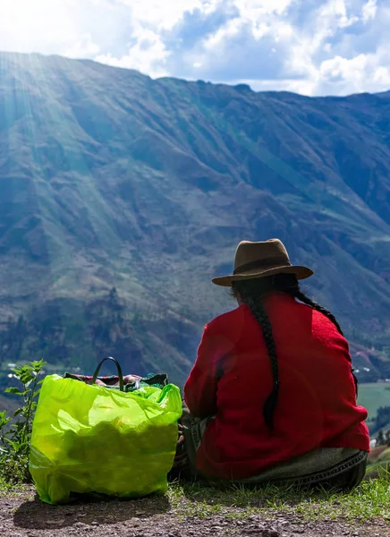 Donna in abiti multicolore peruviano nazionale e in alto cappello marrone feltro si siede dietro vicino alla scogliera e osservare a valle nelle montagne delle Ande — Foto Stock