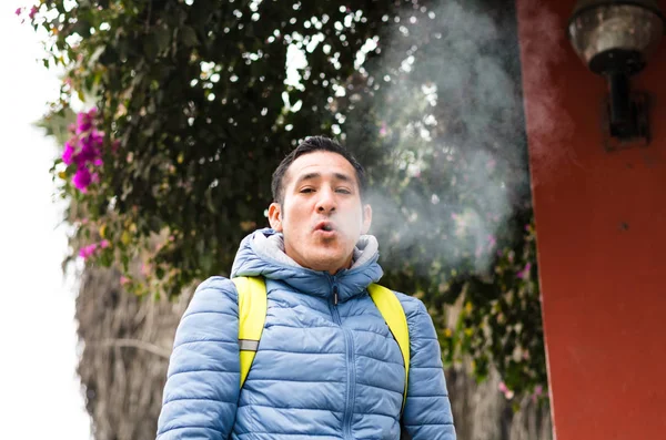 Un hombre con una mochila soplando humo de su boca — Foto de Stock