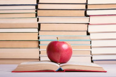 ciltli açık bir kitap üzerinde bir elma kırmızı, arka planda bir sürü kitap yığınları içinde