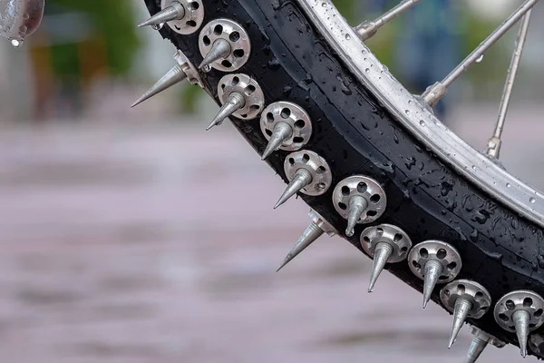 part of the Bicycle wheel covered with large metal spikes in the background of asphalt