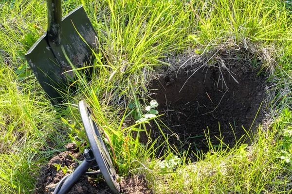 a pit dug in search of treasure, a metal detector and a shovel on a green glade in the summer on a Sunny day