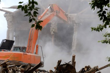tasfiye binanın üzerinde listelenen Ekskavatör bom, duvar çok düştü tekerlekli traktör enkaz ve taşların altında toz, ağaçların arasından görüntülemek