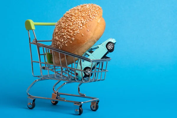 青色の背景色カート スーパー マーケットからハンバーガーとおもちゃの車 青一色のお団子 — ストック写真
