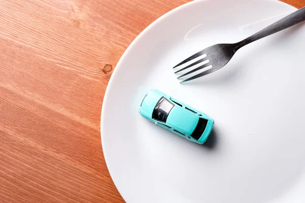in a white plate there is a blue car and a fork for food, a brown wooden background, the composition is located on the left edge