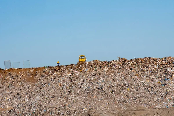 on the mountain of garbage in the dump a big yellow tractor, a lot of sky and a lot of garbage