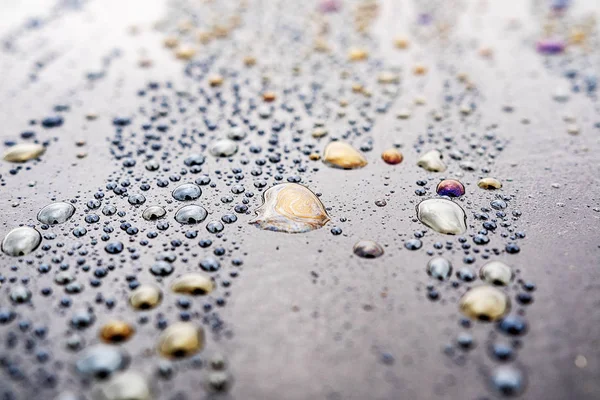 Tracce di prodotti oleosi con trabocco di colore diverso su gocce d'acqua su una superficie scura — Foto Stock
