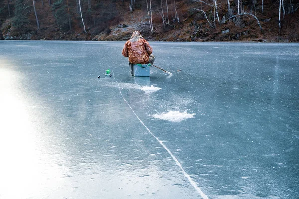 Man sitting on the ice fishing next to him crack on clear ice — Stock Photo, Image