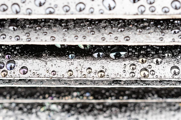 Gocce di pioggia sulla superficie a gradini nera, la figura umana si riflette nelle gocce — Foto Stock
