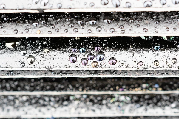 Gocce multicolori di prodotti petroliferi su fondo nero, grandi gocce di pioggia sui gradini del loro materiale nero, le gocce riflettevano l'uomo — Foto Stock