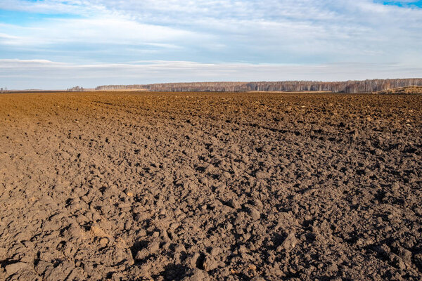 вспаханное поле до линии горизонта под небом с облаками, большими кусками земли и сухой травой
