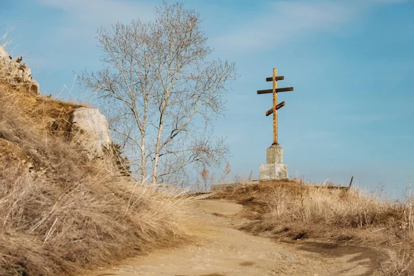 大きな木製のオーソドックスな十字架は、葉のない木の近くの丘の上に設定されています — ストック写真
