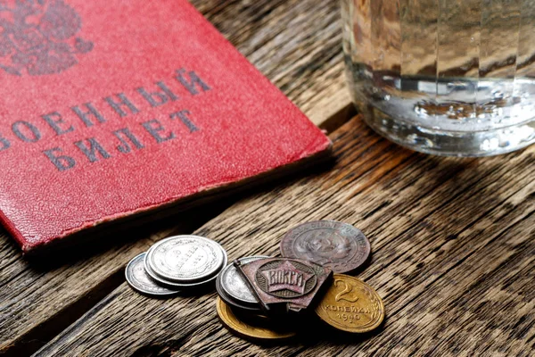 Inscription in Russian military ID on a wooden table next to a glass of vodka and old Soviet coins