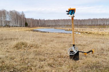 gölün ve tarlanın arka planında kürek metal dedektörü üzerinde yere kazıklı kürek vardır, alanında çıplak bir lem ve kuru çim ile bahar yara