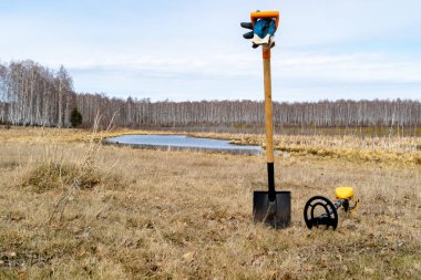 bahar alanında, bir kürek ve üzerinde yatan bir metal dedektörü yere itme vardır, zdanya planı göl ve orman