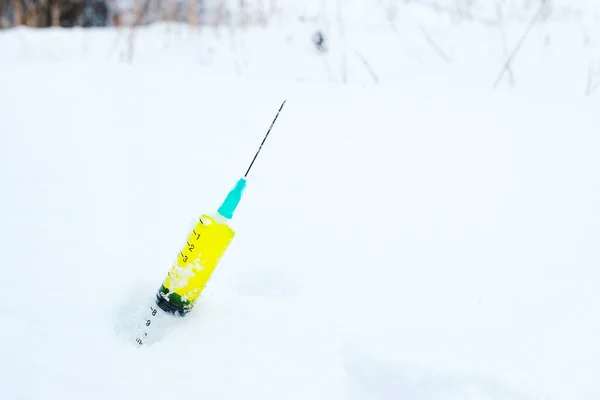 Una siringa con liquido sconosciuto gettata nella neve con un ago alzato — Foto Stock