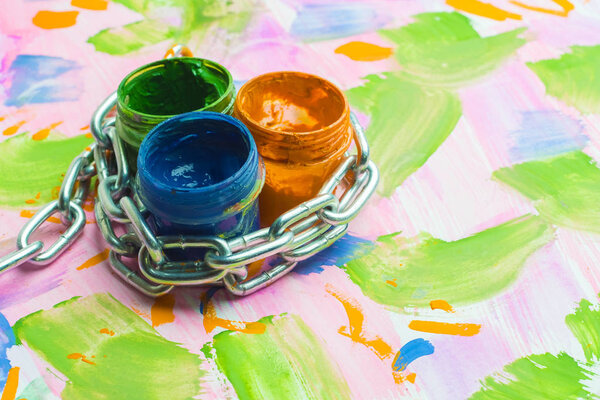 ban on creativity, three cans of paint are entwined with a metal chain, a multicolored background