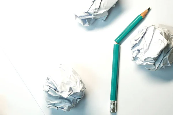 Un lápiz verde roto sobre un fondo de papel blanco cerca hay tres hojas de papel arrugadas — Foto de Stock