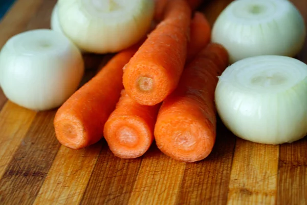 Морква і цибуля очищені, але не нарізані на ріжучій дошці на дерев'яному фоні, свіжі овочі для приготування їжі, натуральні з саду — стокове фото