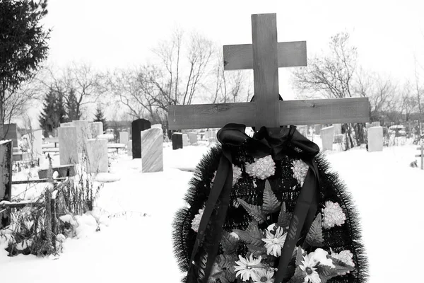 前景の冬の間に墓地は、背景の墓石、村の墓地、黒と白で、人工花の花輪を持つ墓の上の十字架 — ストック写真