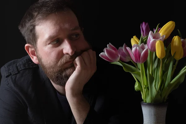 Hombre clave oscura mirando un ramo de tulipanes en un jarrón — Foto de Stock