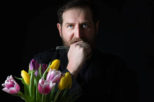 Barbudo hombre con una pluma estilográfica en el fondo en el fondo tulipanes primer plano oscuro — Foto de Stock