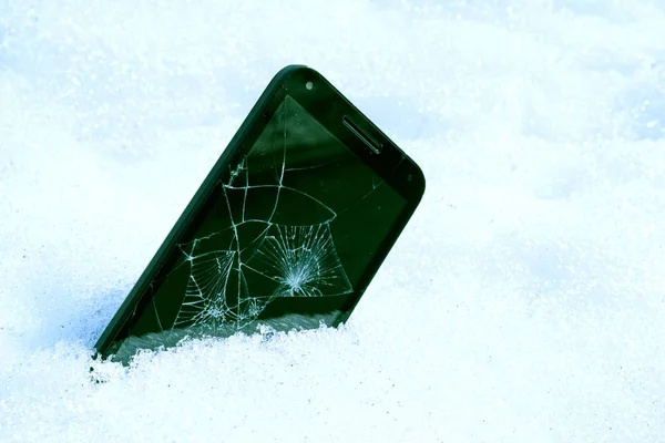 inserted into the snow unnecessary smartphone with a broken screen, blue tinted picture