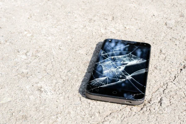 on the gray dirty asphalt among the stones is a smartphone with a broken screen