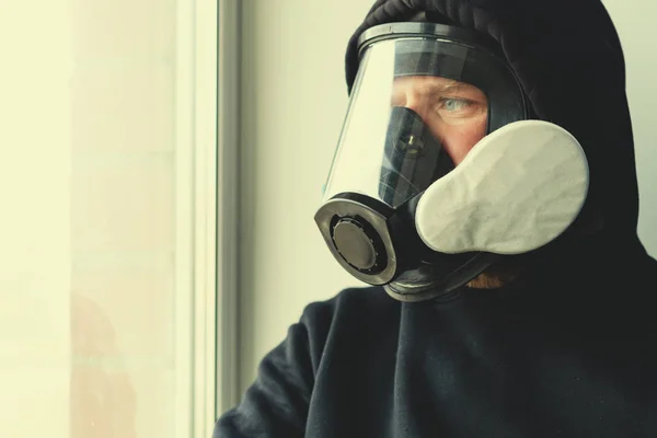 Un homme dans un masque à gaz est assis en face de la fenêtre et regarde derrière la vitre — Photo