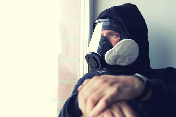 Un homme avec un masque à gaz regardant par la fenêtre a croisé les mains au premier plan — Photo