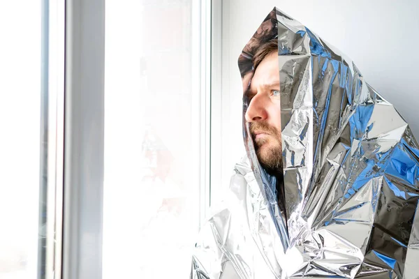 Un uomo con la barba è avvolto in un grande materiale lucido e guarda fuori dalla finestra — Foto Stock