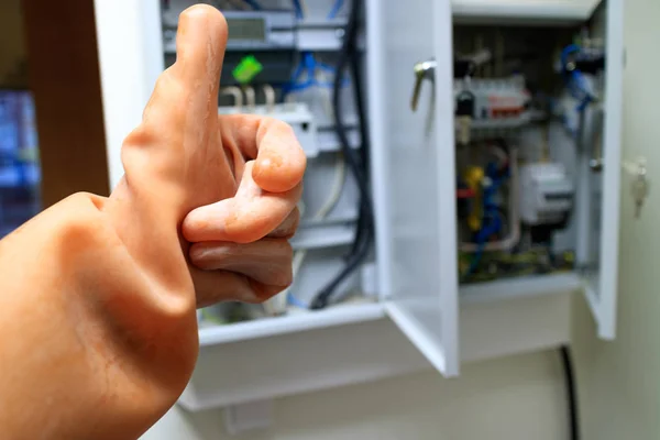 An open electric box with electro-automatics and a hand in a dielectric silicone glove with a raised thumb up — Stock Photo, Image