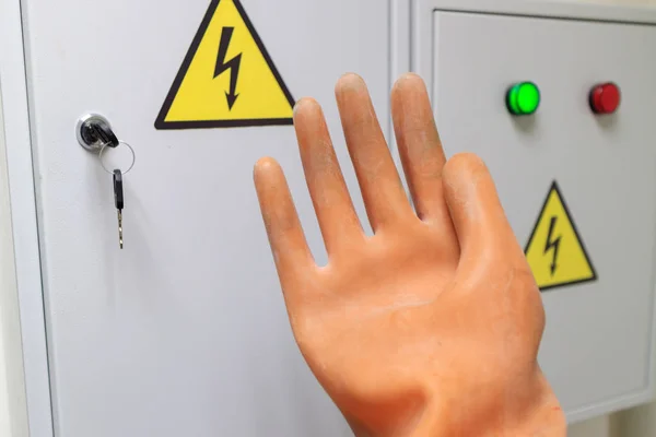 Rubber insulating glove in front of the doors of the electric flap on the caution sign electricity — Stock Photo, Image