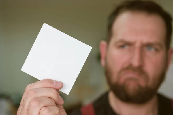 Una hoja de papel blanco en forma cuadrada en blanco en la mano en el fondo —  Fotos de Stock