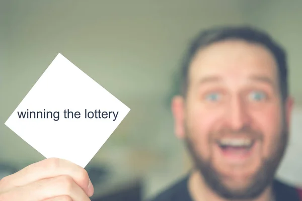 the man won the lottery holds the lucky ticket in his hand in the foreground background blurred out of focus face