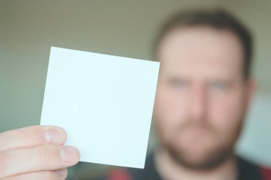 sakallı ciddi bir adam önünde temiz bir kare kağıt parçası tutar