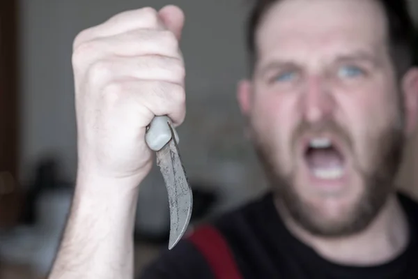 Screaming man with a curved knife in his hand in the background out of focus in the foreground knife old — Stock Photo, Image