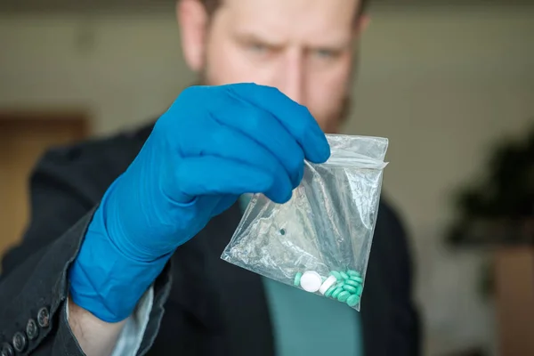 Um homem com barba está segurando um pacote suspeito de pílulas com as mãos enluvadas — Fotografia de Stock
