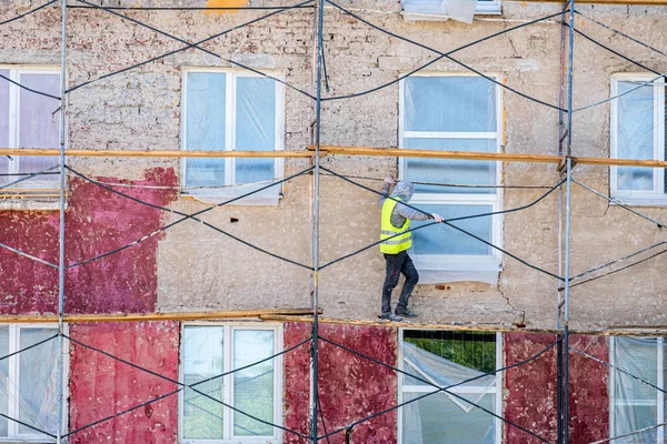 Рухаючись вздовж стіни працівника в жовтому жилеті на тлі ремонтованого будинку — стокове фото