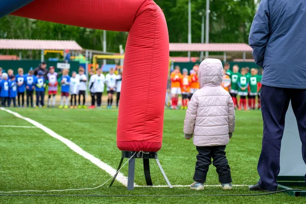 Un niño en el borde del campo de fútbol mirando al equipo en el lado opuesto al lado de un adulto —  Fotos de Stock
